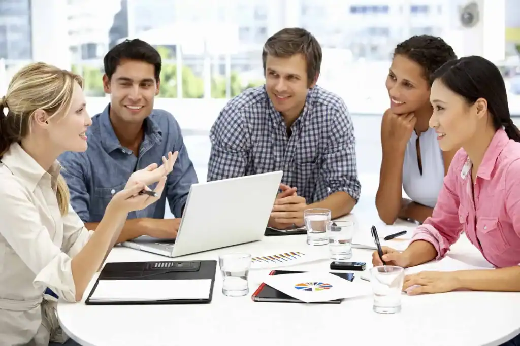 A diverse team of professionals collaborating around a table with a laptop, illustrating Delaware Digital
